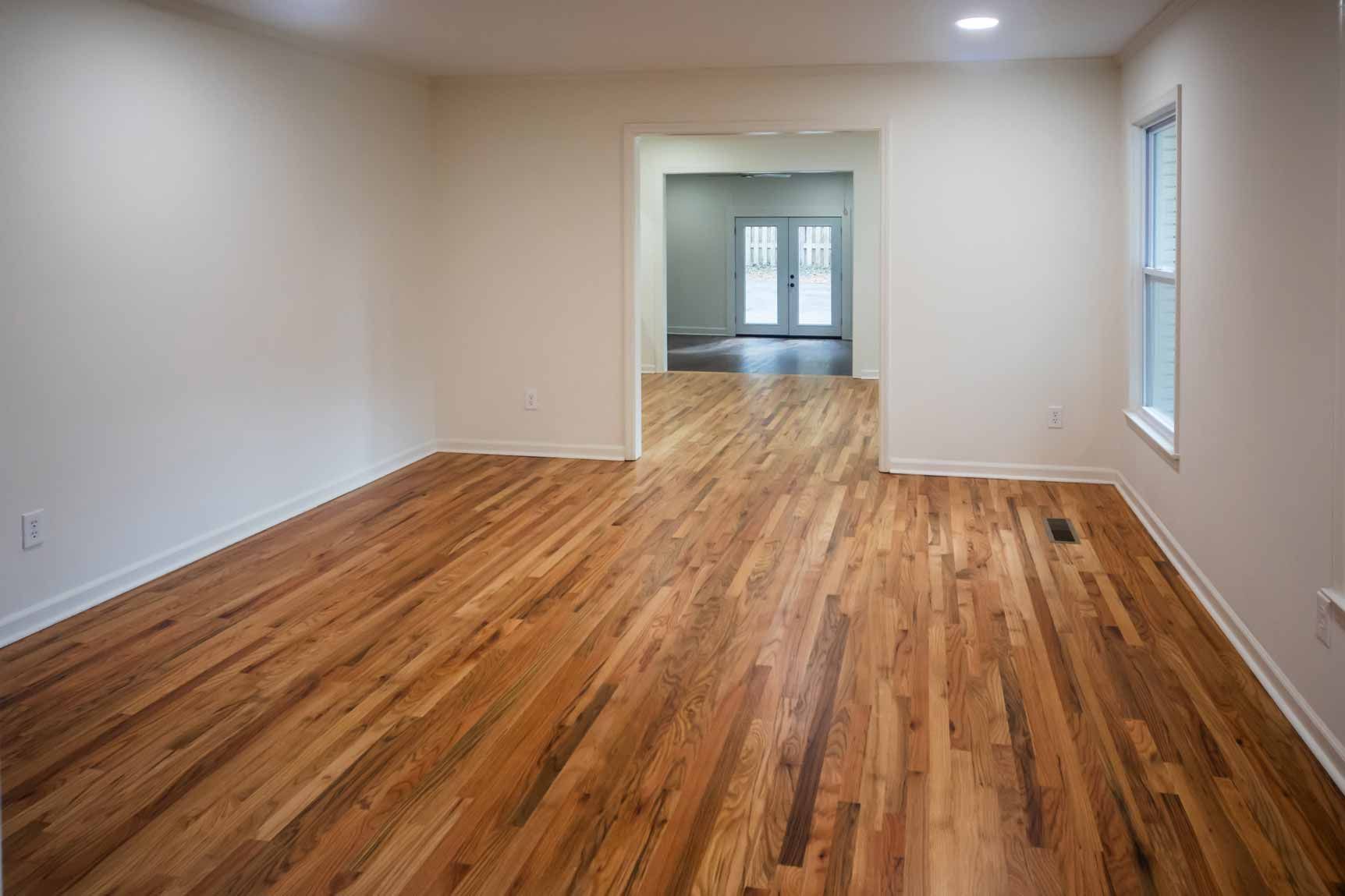 Empty living room with hardwood floors, white walls, and windows at each end