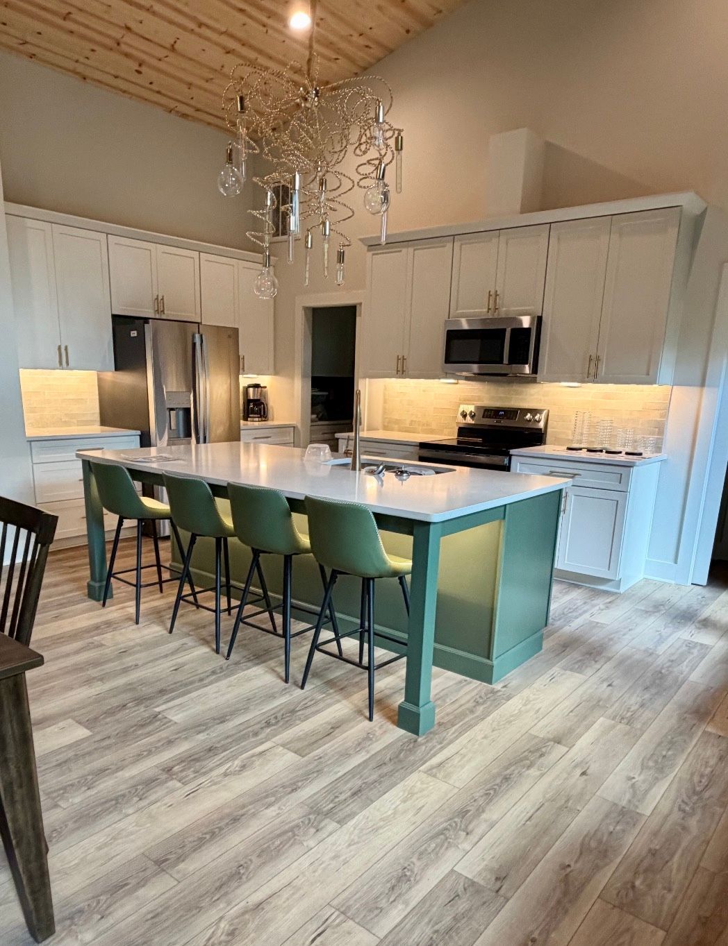 Bright modern kitchen with teal island, green stools, stainless appliances, and white cabinetry