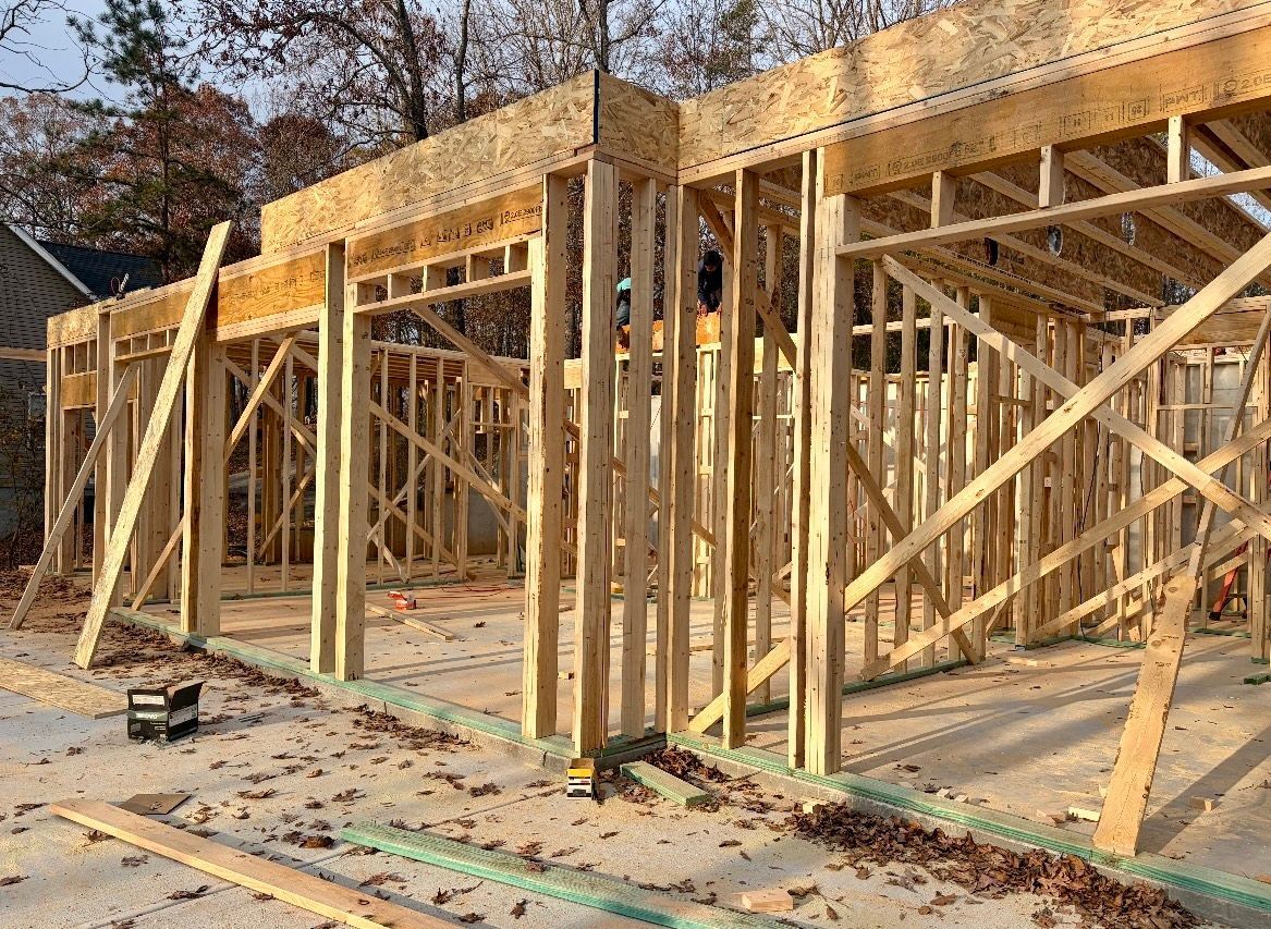 Wooden house framing under construction with exposed studs and trusses on a concrete slab