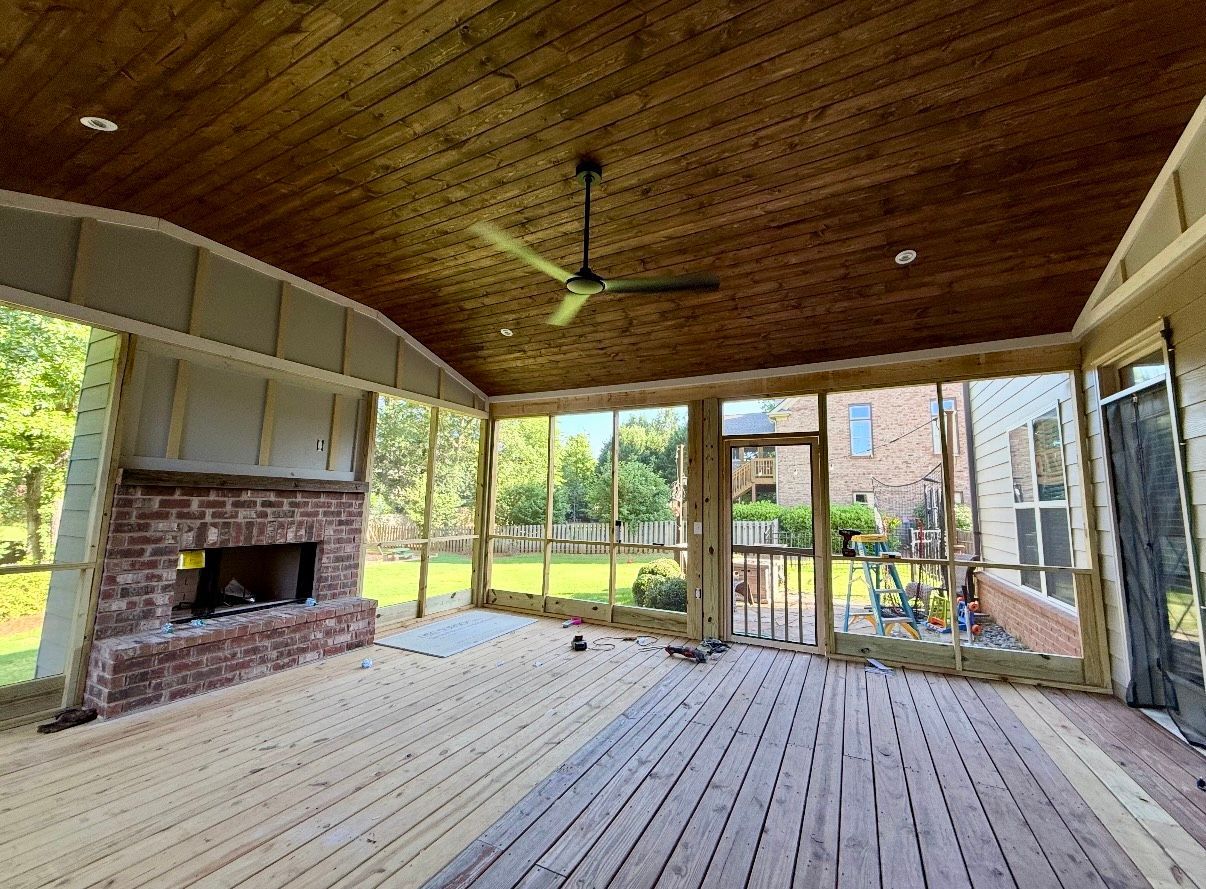 Covered wooden porch with brick fireplace, ceiling fan, and open yard views