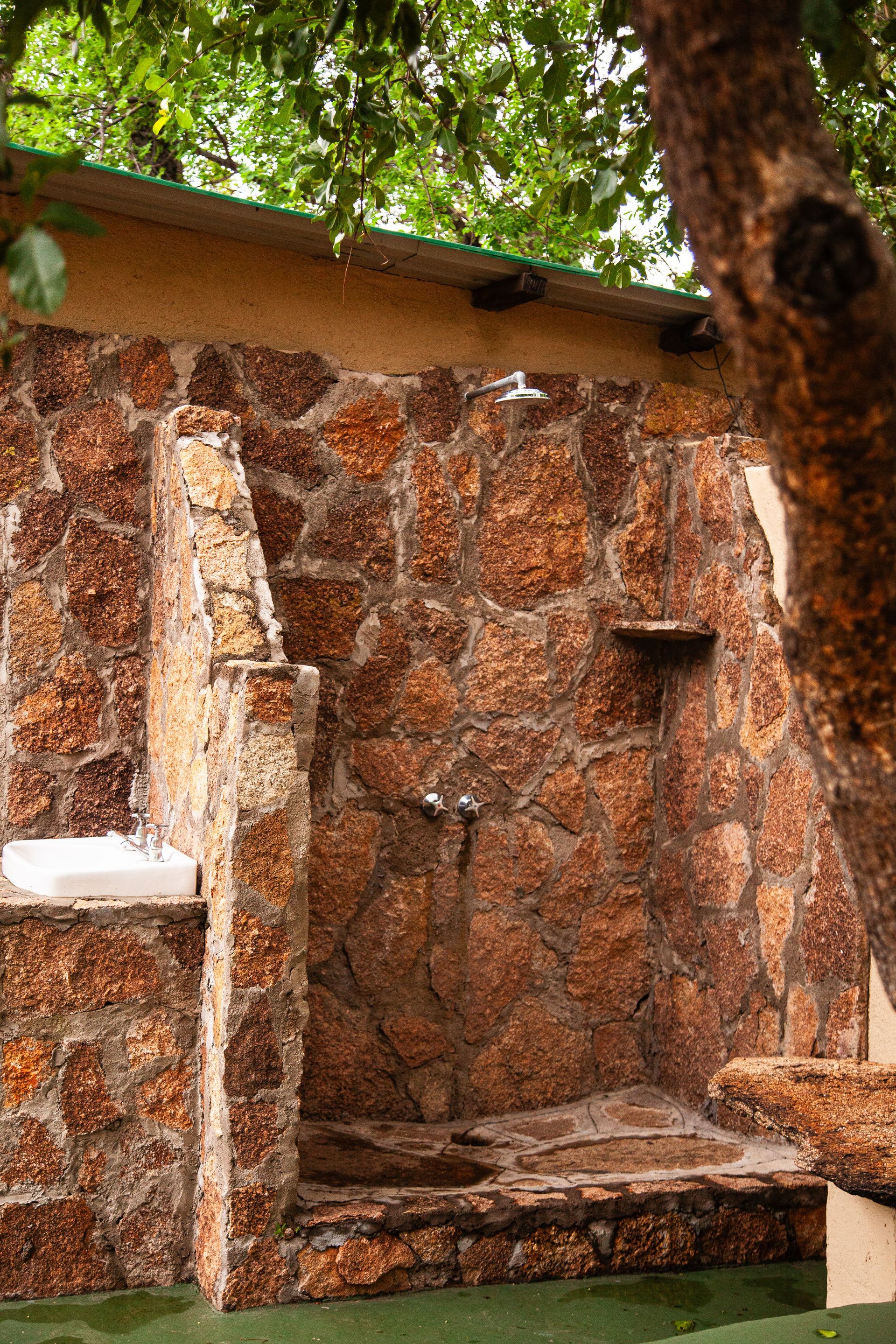 Outdoor shower with rough, red-brown stone walls, chrome fixtures, and a small built-in shelf.