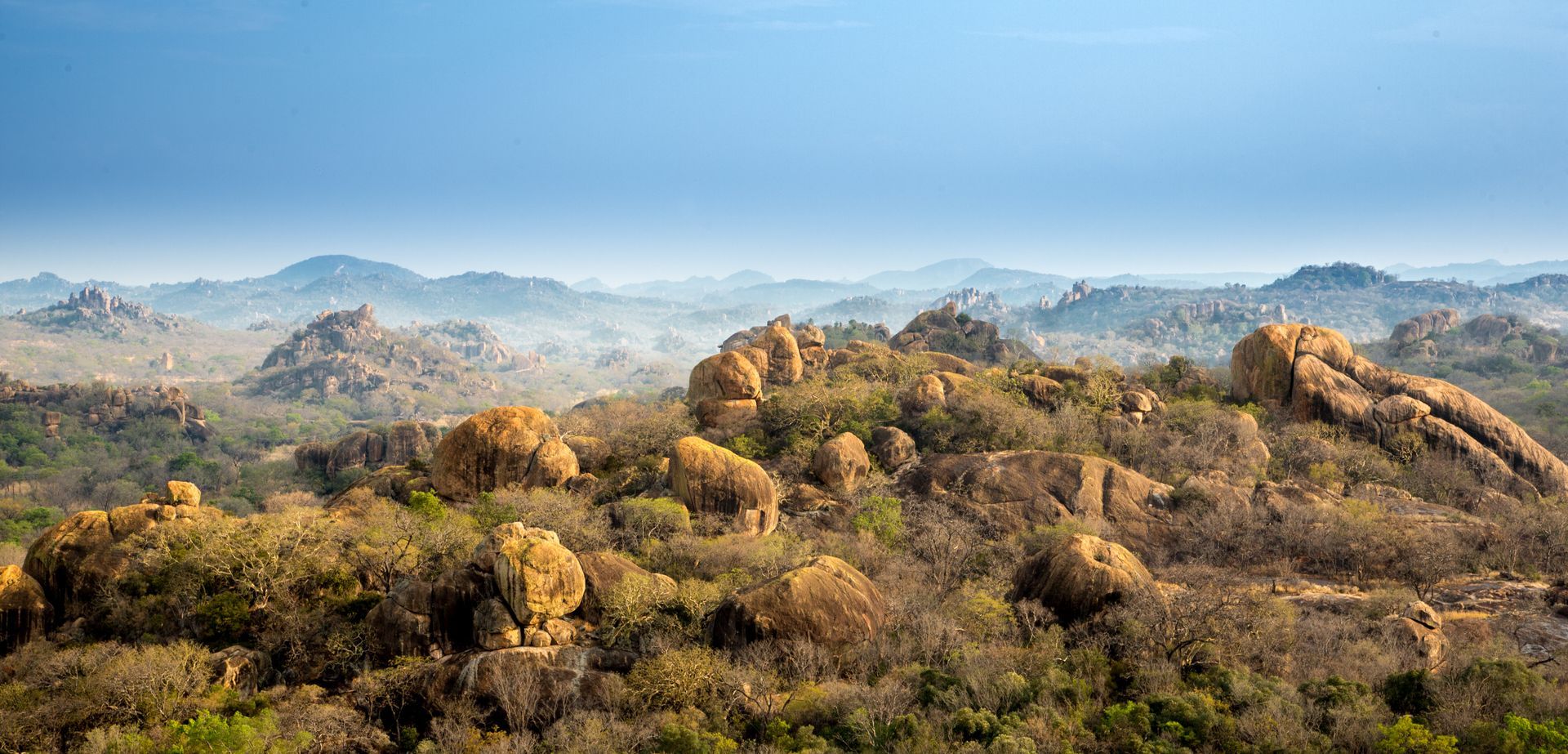 A landscape of rocky hills covered with dry vegetation under a hazy blue sky.