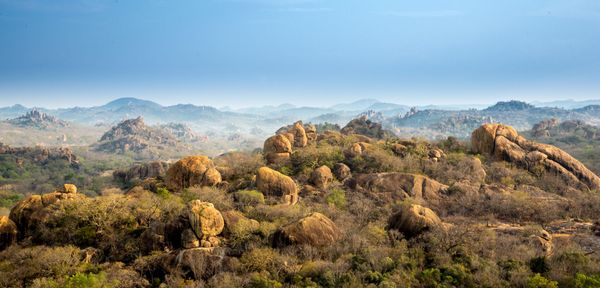 A landscape of rocky hills covered with dry vegetation under a hazy blue sky.