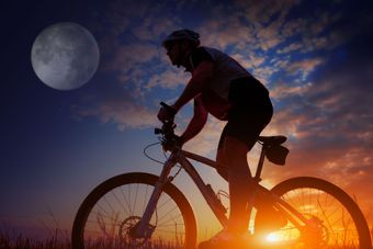 Bici al tramonto con il sole e la luna sullo sfondo