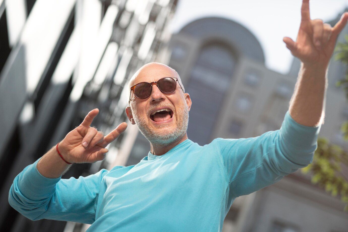 Un hombre mayor con gafas de sol está haciendo un gesto de rock and roll con las manos en el aire.