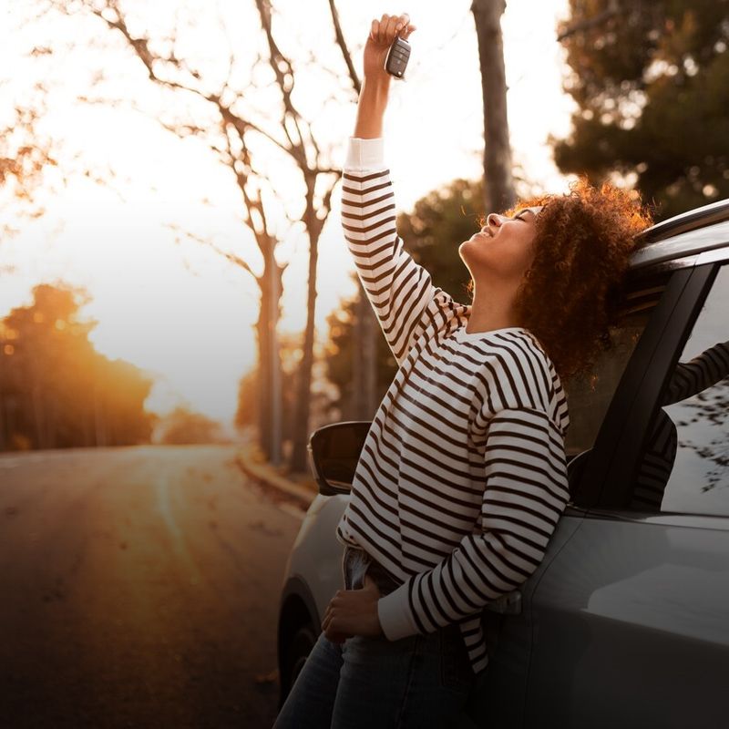 Una mujer está apoyada contra un automóvil sosteniendo una llave.