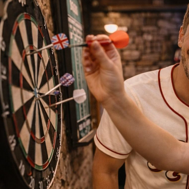 Person throwing darts at a dartboard in a pub, with darts stuck on the board.