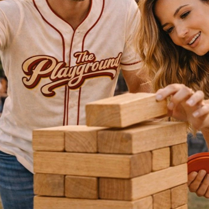 Two people stacking wooden blocks on a tabletop, with a smiling woman reaching toward the tower