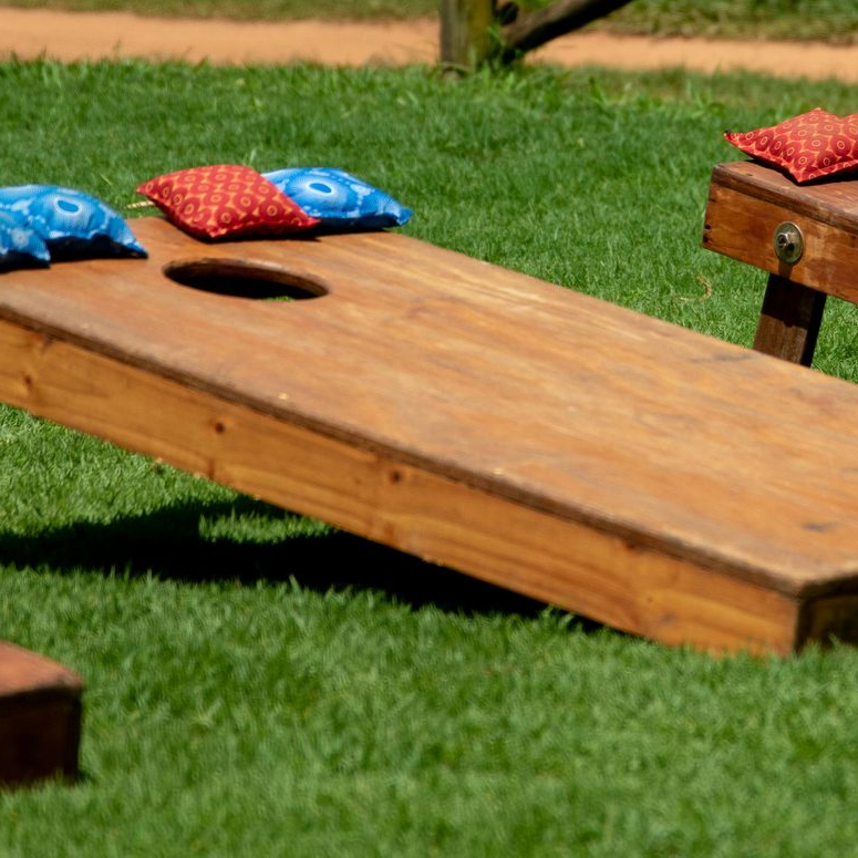 Wooden cornhole board on grass with red and blue bean bags nearby
