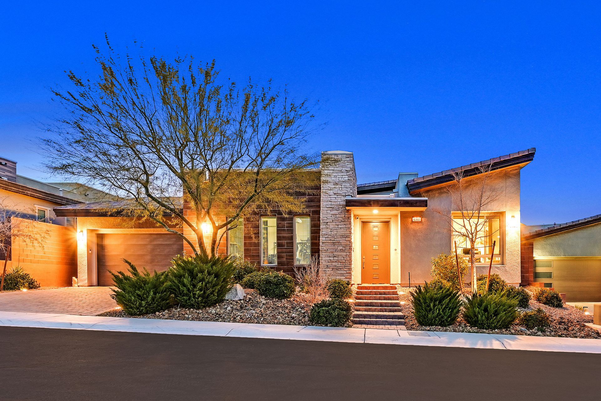 Modern home exterior with garage, stucco walls, and desert landscaping at dusk.