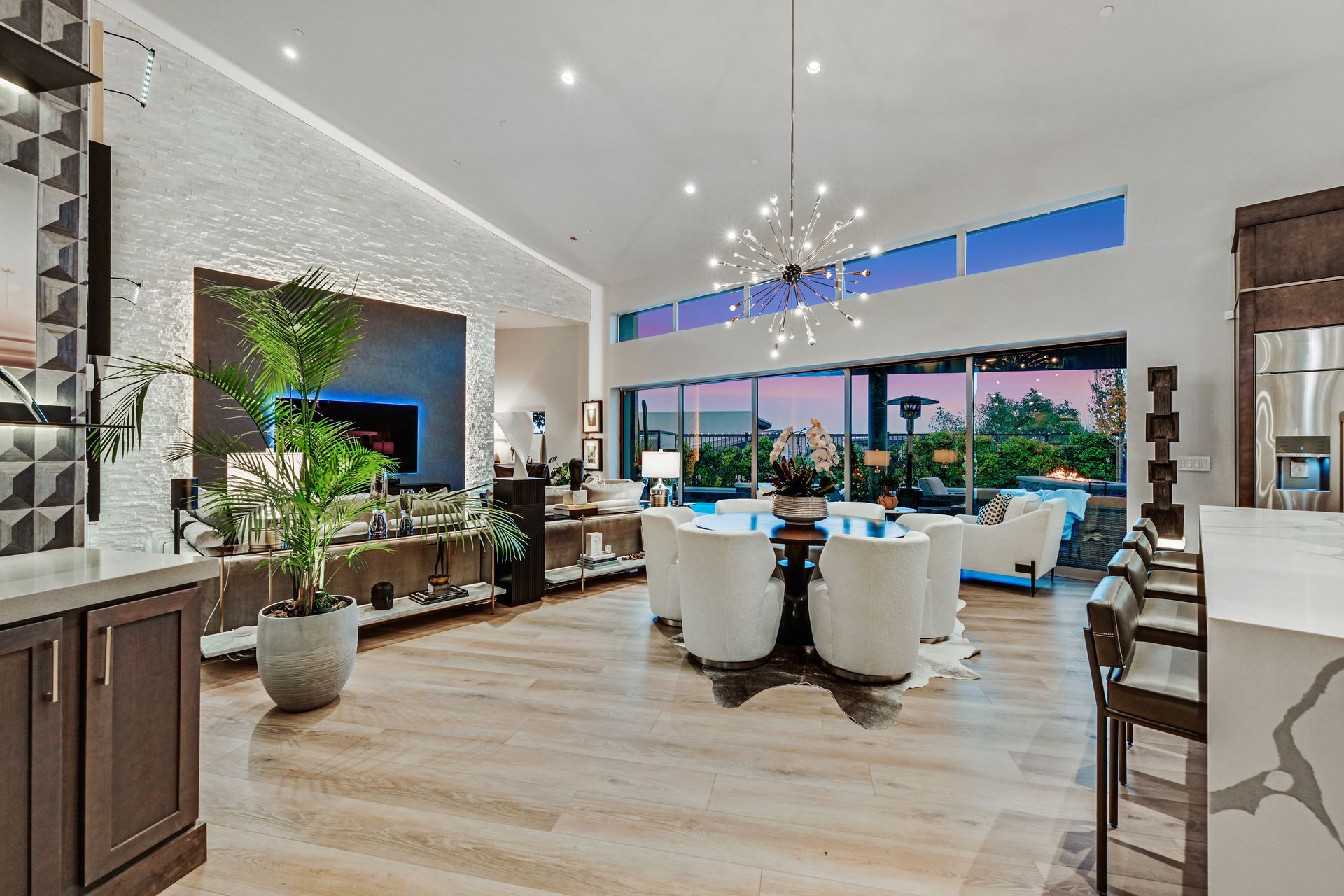 Luxurious open-concept living space with dining area, large windows, wood floors, and a modern chandelier.