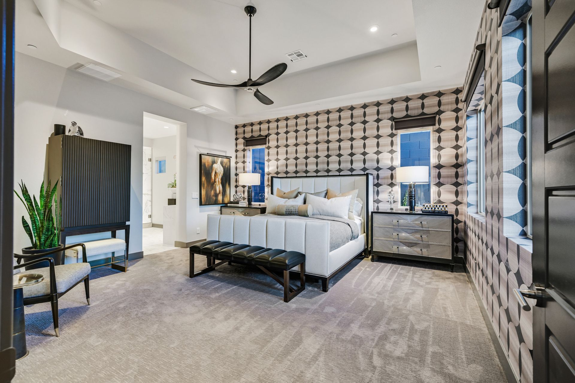 Spacious, modern bedroom with patterned wallpaper, large bed, black bench, and a walk-in closet.
