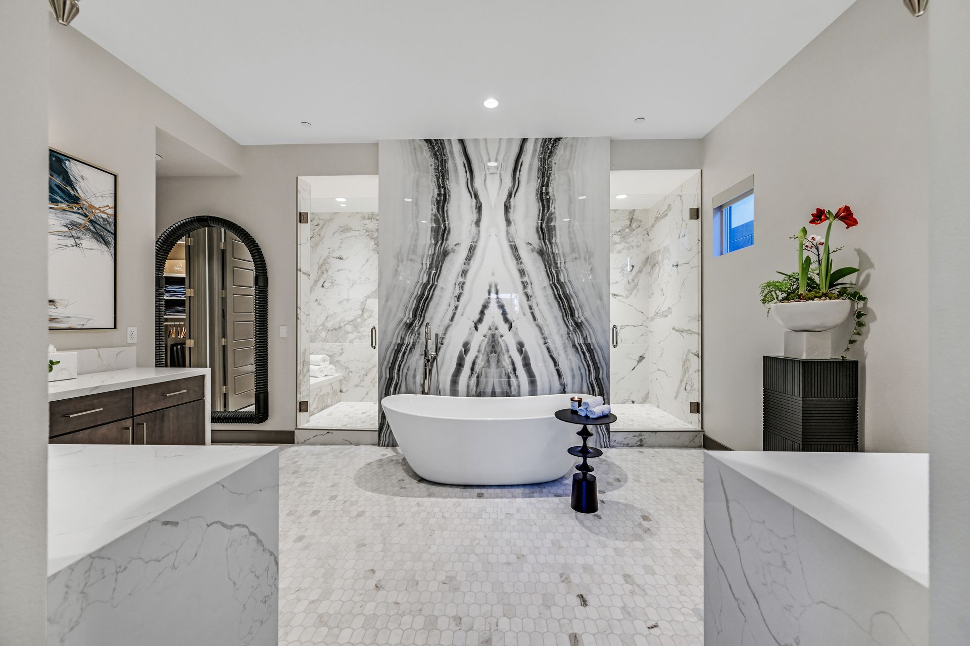 Luxurious bathroom with a marble accent wall, soaking tub, two showers, and a vanity.