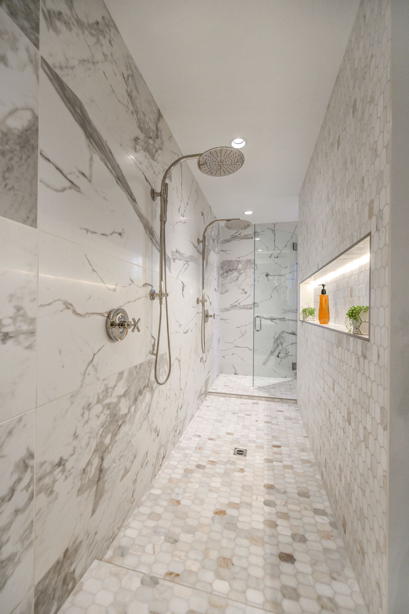 Luxurious marble-tiled shower with a rain showerhead, glass doors, and a built-in shelf with toiletries.