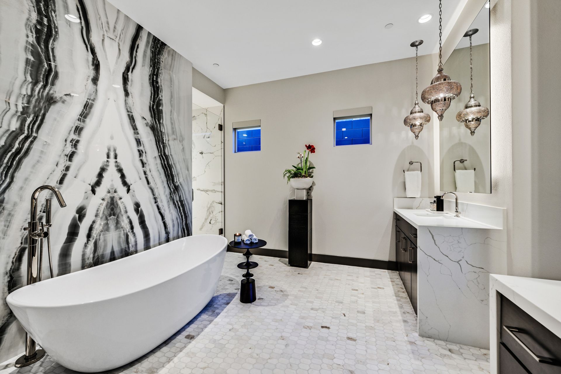 Luxurious bathroom with a white oval tub, patterned marble wall, and two pendant lights.