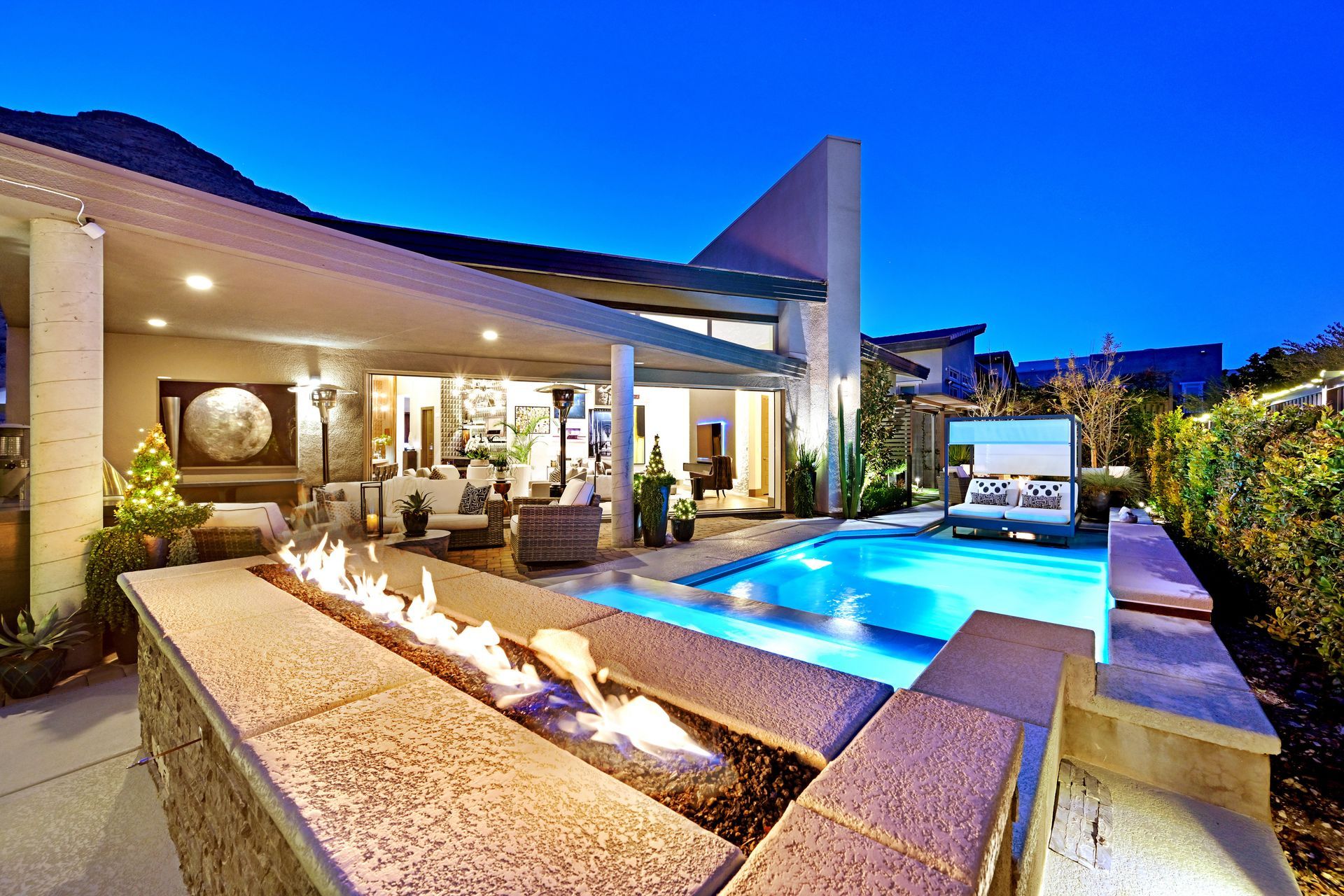 Backyard with a pool, fire pit, patio furniture, and modern house at twilight.