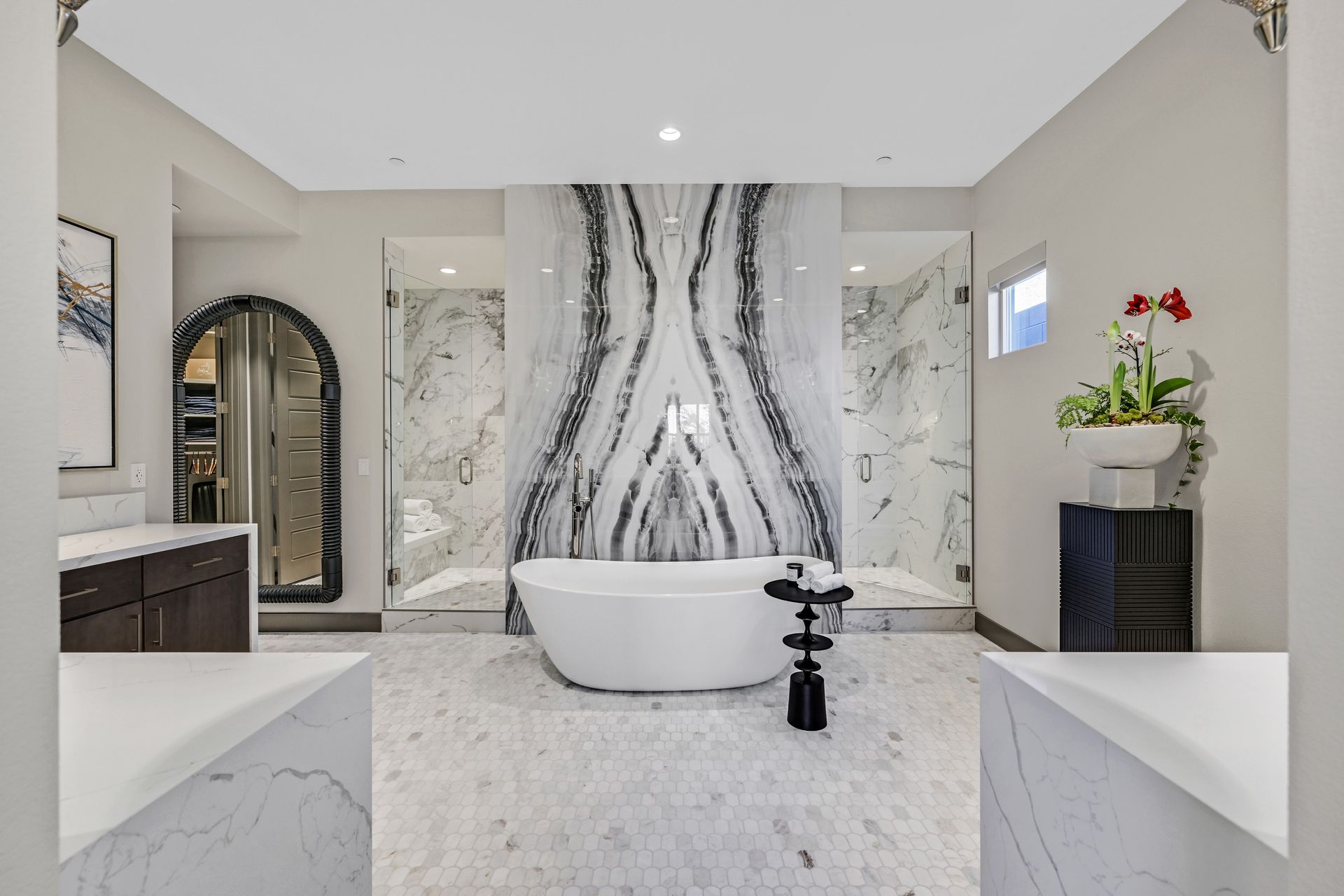 Luxurious bathroom with marble walls, freestanding tub, and two glass showers.