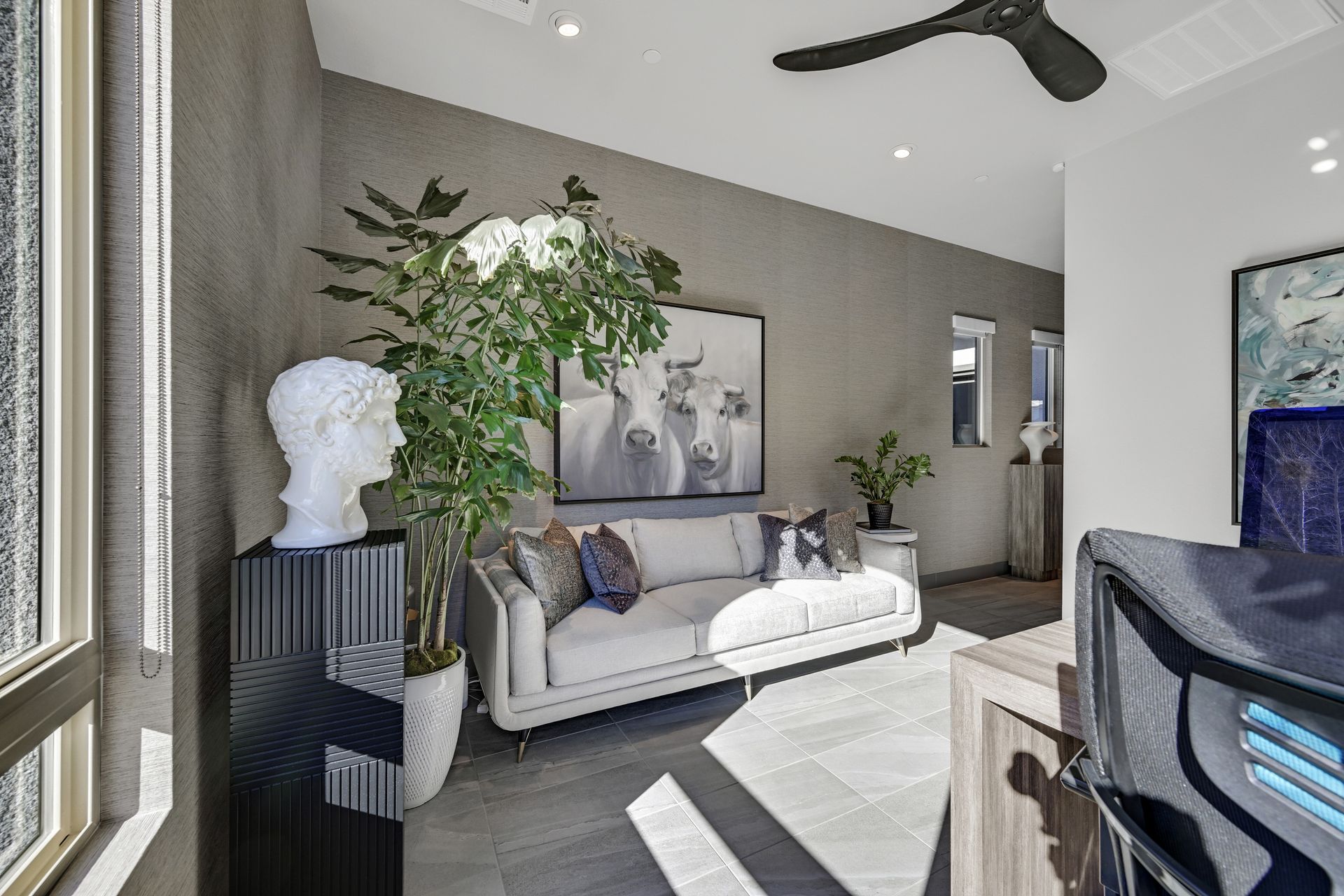 Home Office with a gray wall, sofa, large plant, and artwork. Sunlight streams in.