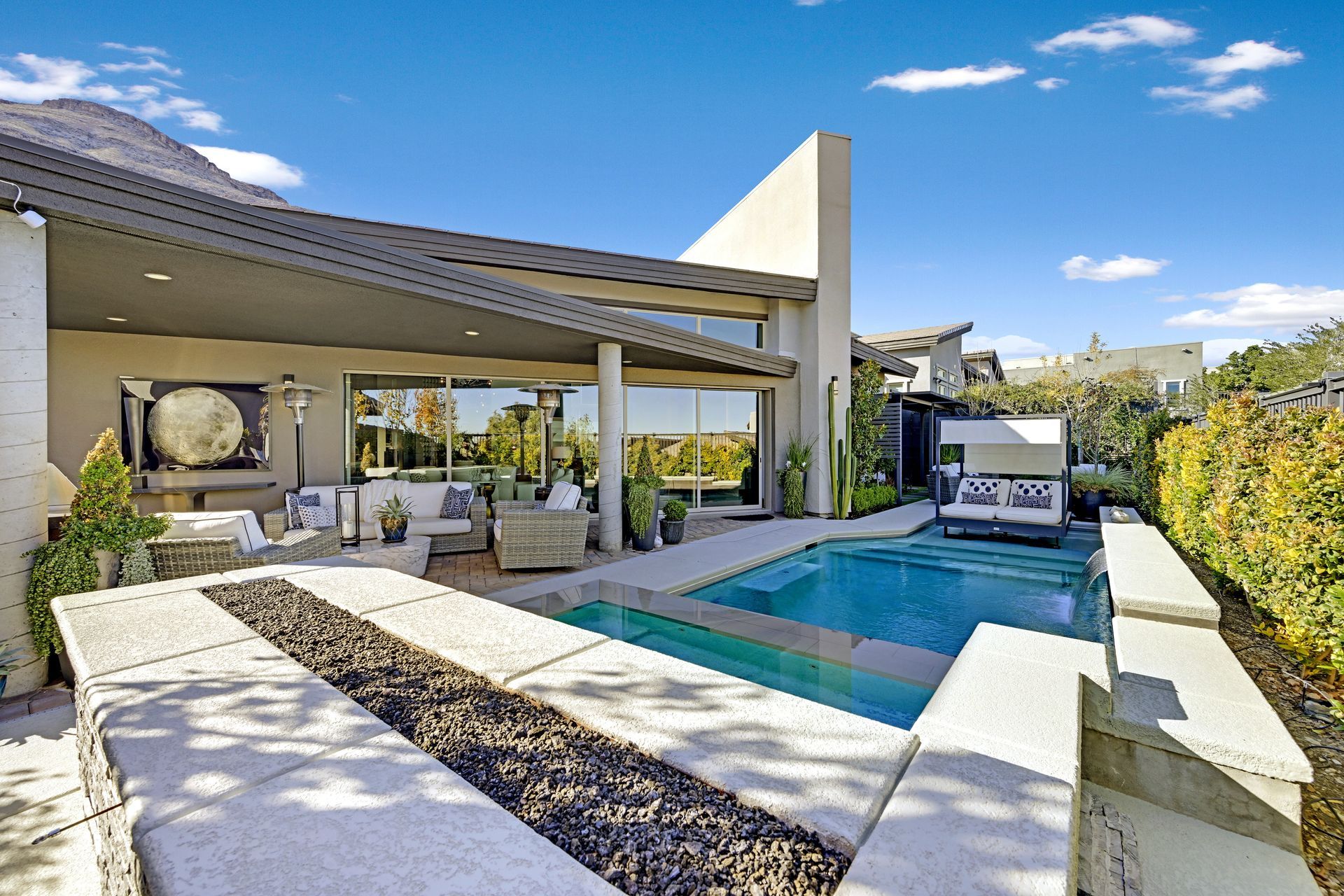 Luxury home backyard with pool, patio, fire pit, and mountain view, under a sunny blue sky.