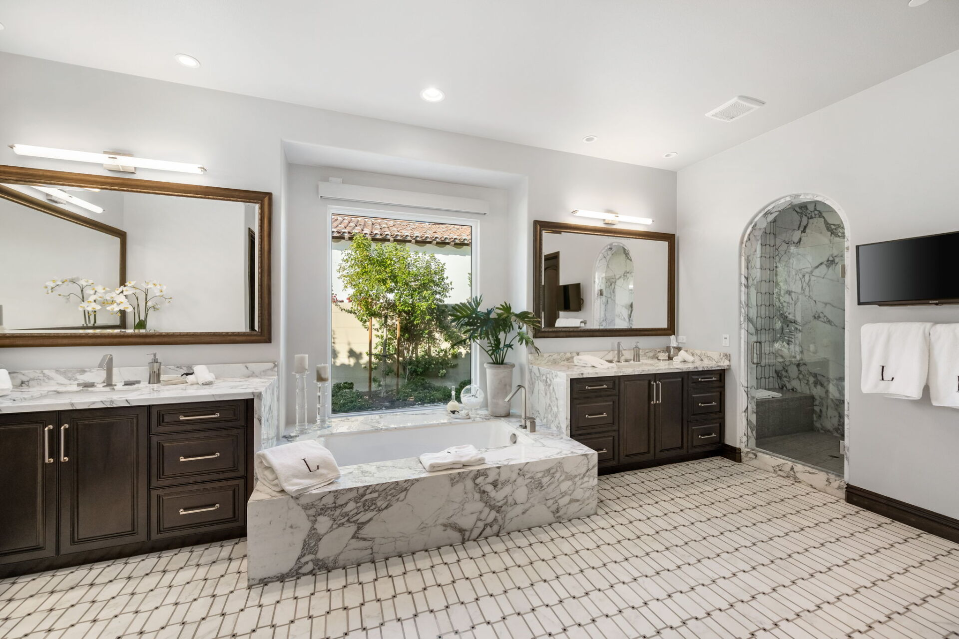 Spacious luxury bathroom with marble bathtub, dark wood vanities, and outdoor view.