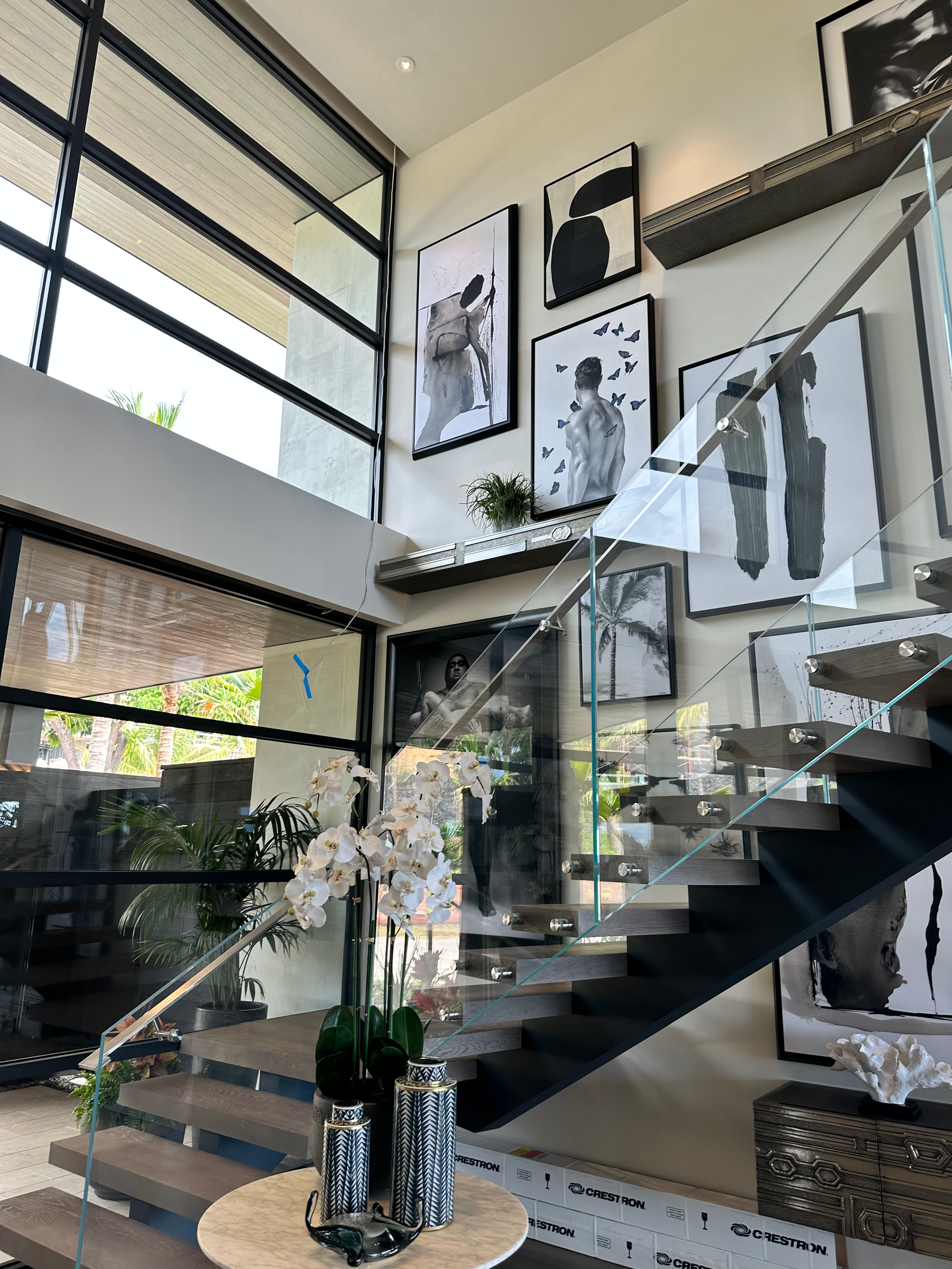 Modern staircase with abstract art, glass railings, and orchid arrangement.