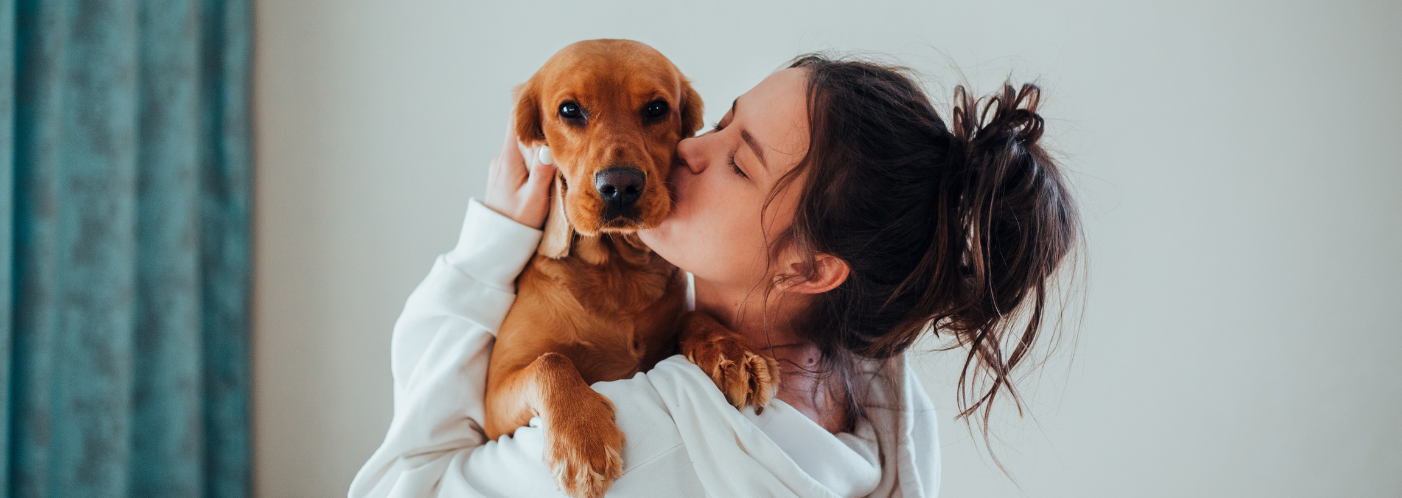 A woman is kissing a puppy on the nose.