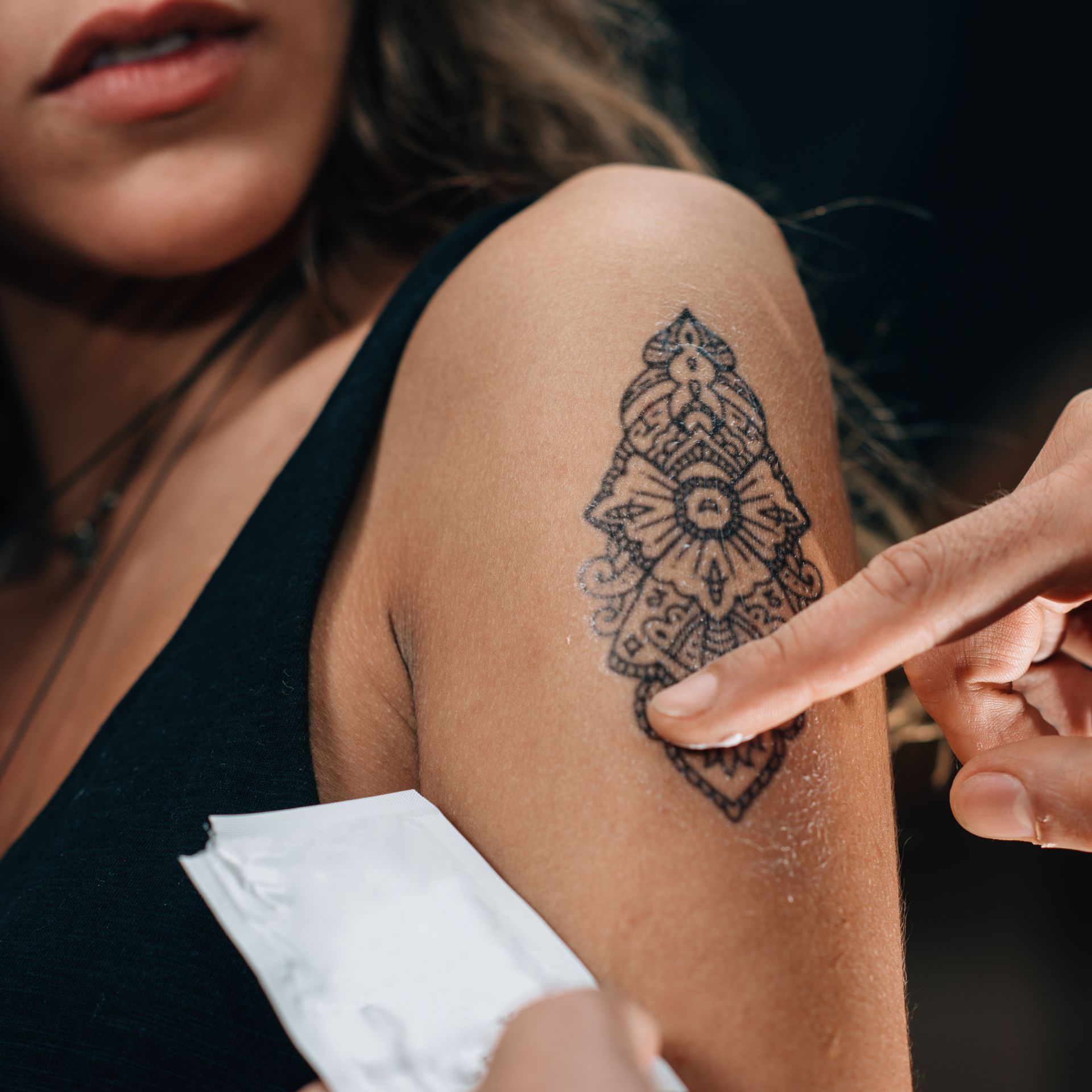Person pointing at a temporary tattoo on another person's arm. Black design on light skin.
