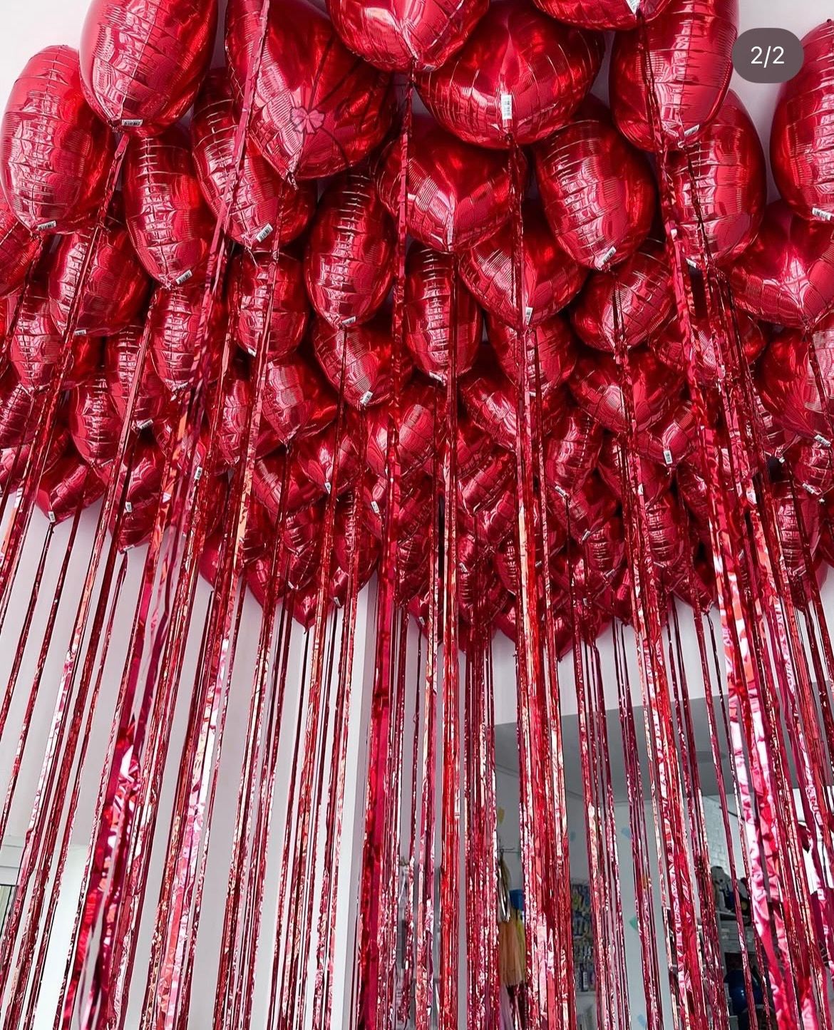 Red heart-shaped balloons and shiny red fringe hang from a ceiling.