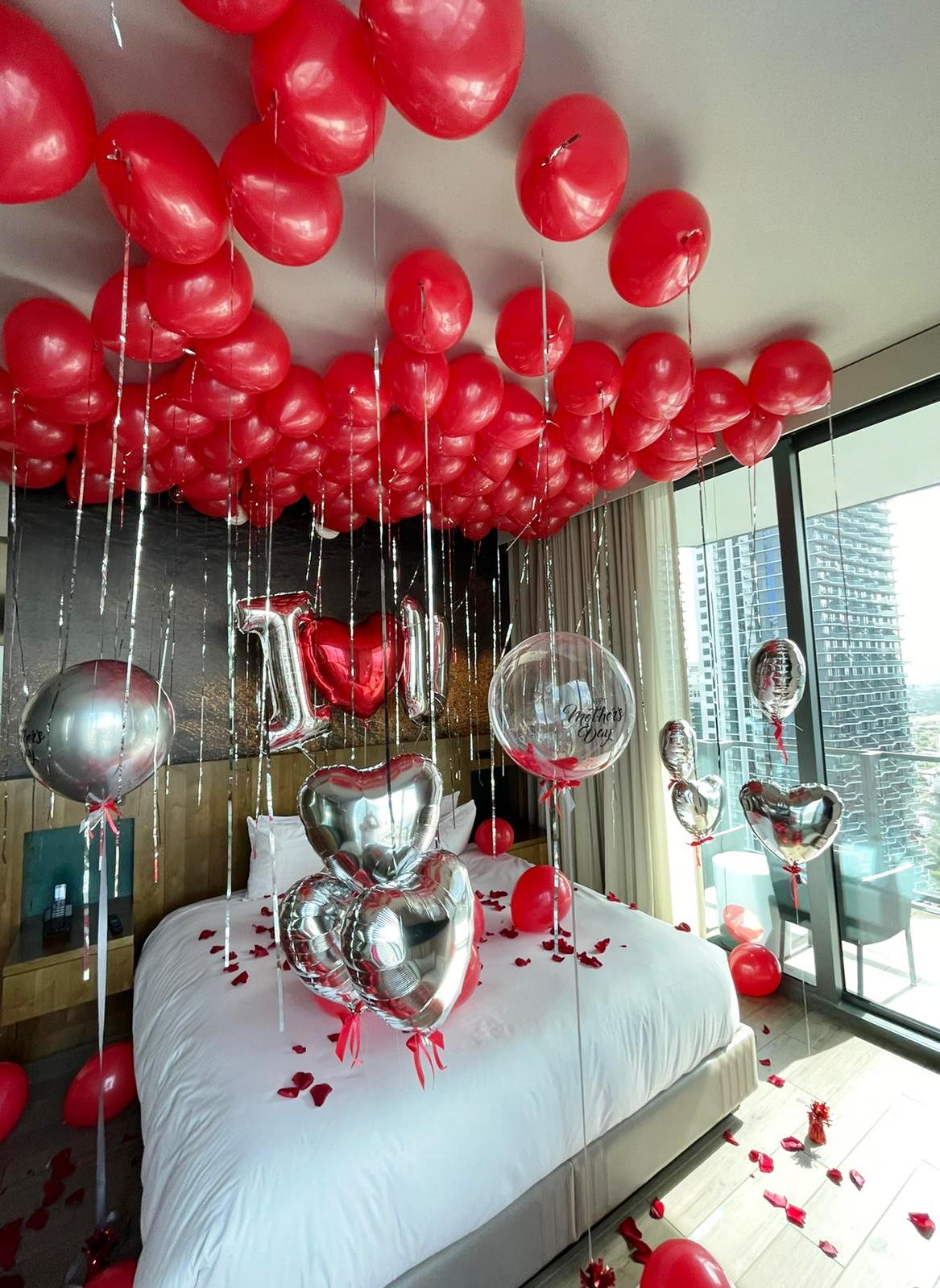 Bedroom decorated with red balloons and heart-shaped balloons for a celebration.
