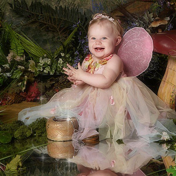 A baby dressed as a fairy is sitting on a mushroom.