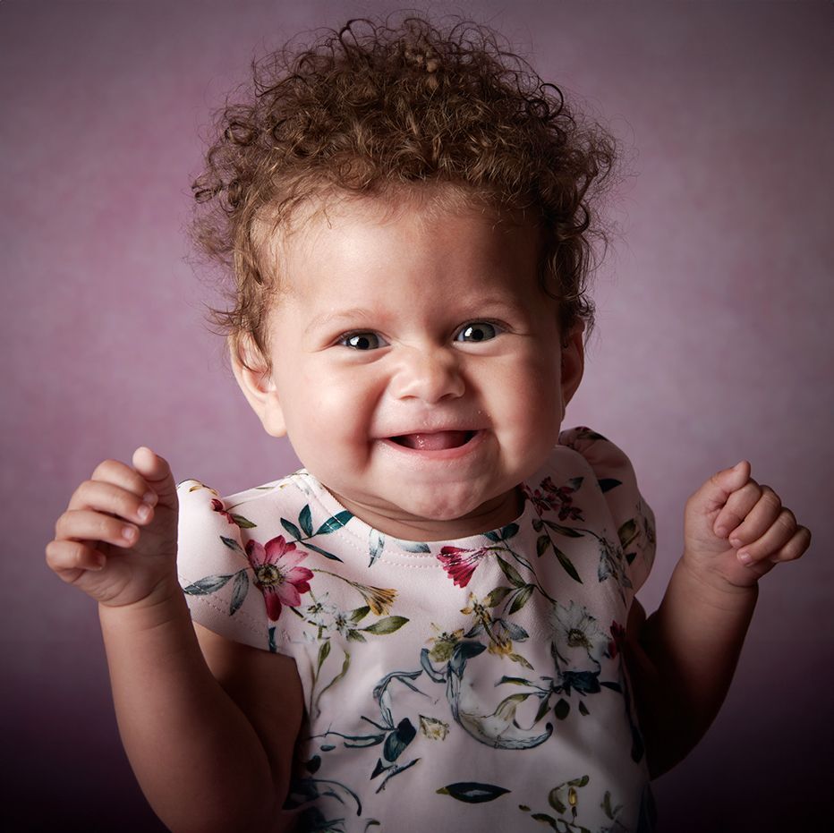 Curly-haired baby smiling in a floral dress — Watch Me Grow baby photoshoot at Oakley Studios, Luton, Bedfordshire
