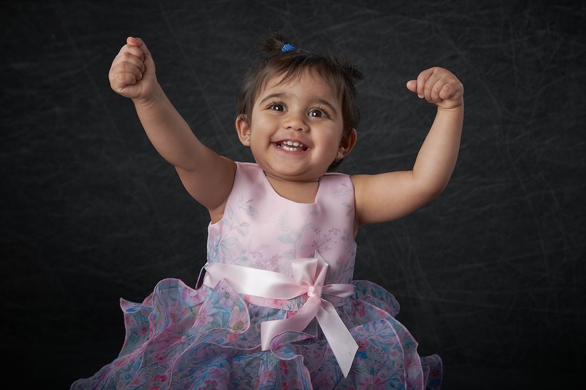 Happy little girl raising her arms and smiling during a children's portrait session at Oakley Studios, Luton