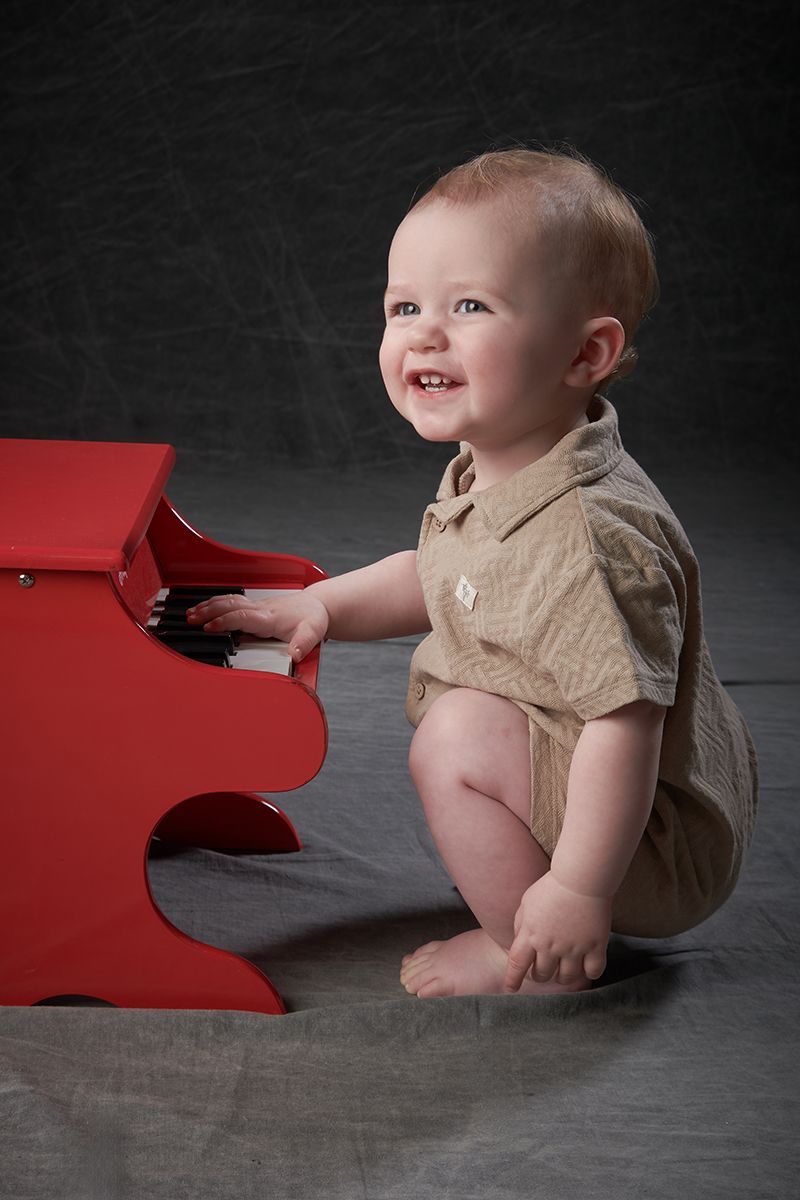 One-year-old boy sitting at a toy red piano during a toddler portrait session at Oakley Studios, Luton