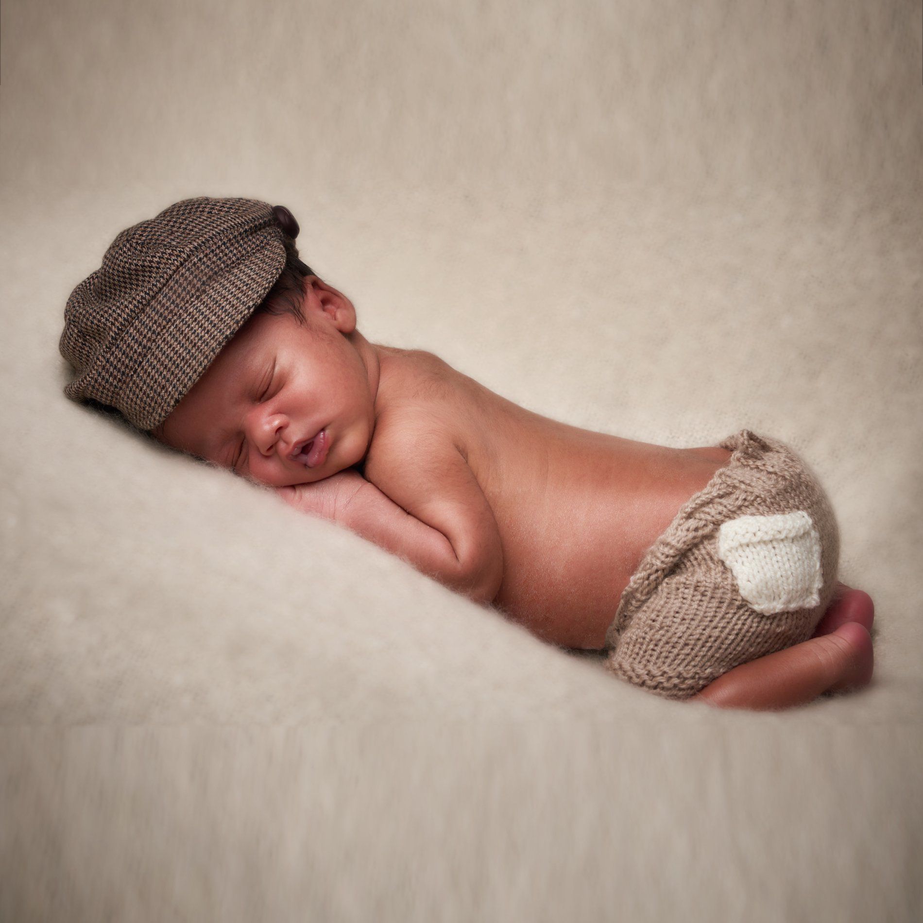 A baby wearing a hat and shorts is sleeping on a blanket