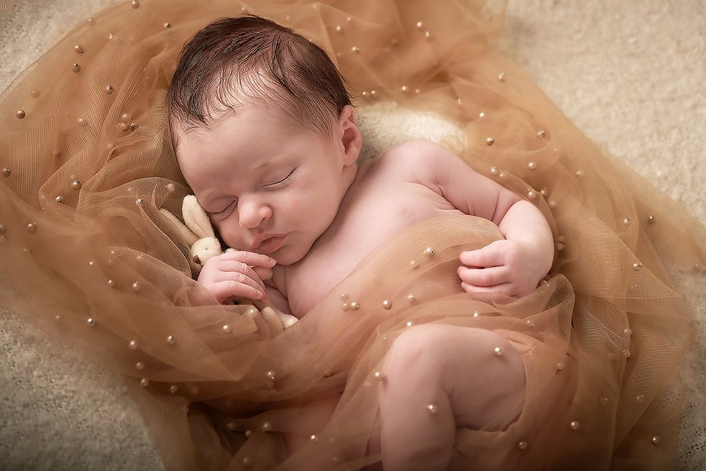 Sleeping newborn baby on cream background — certified newborn photography at Oakley Studios, Bedfordshire