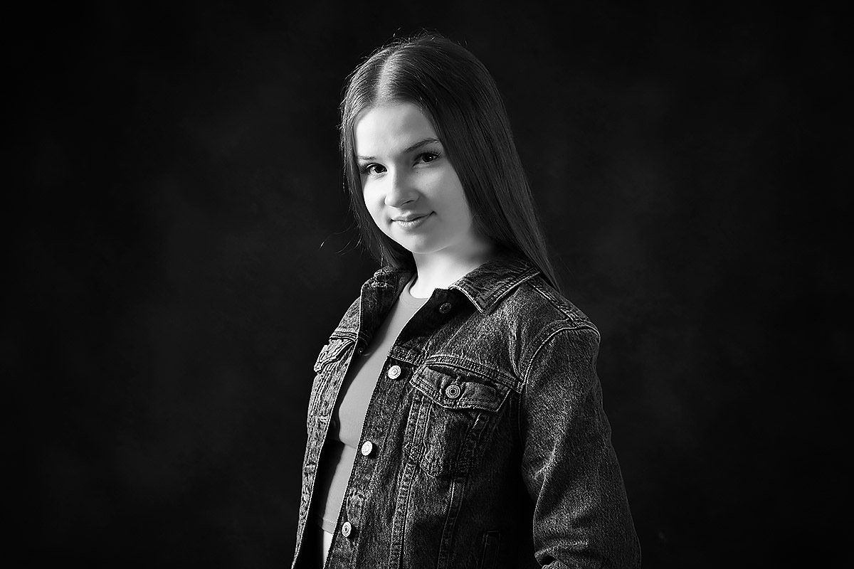 A black and white photo of a young girl wearing a denim jacket.