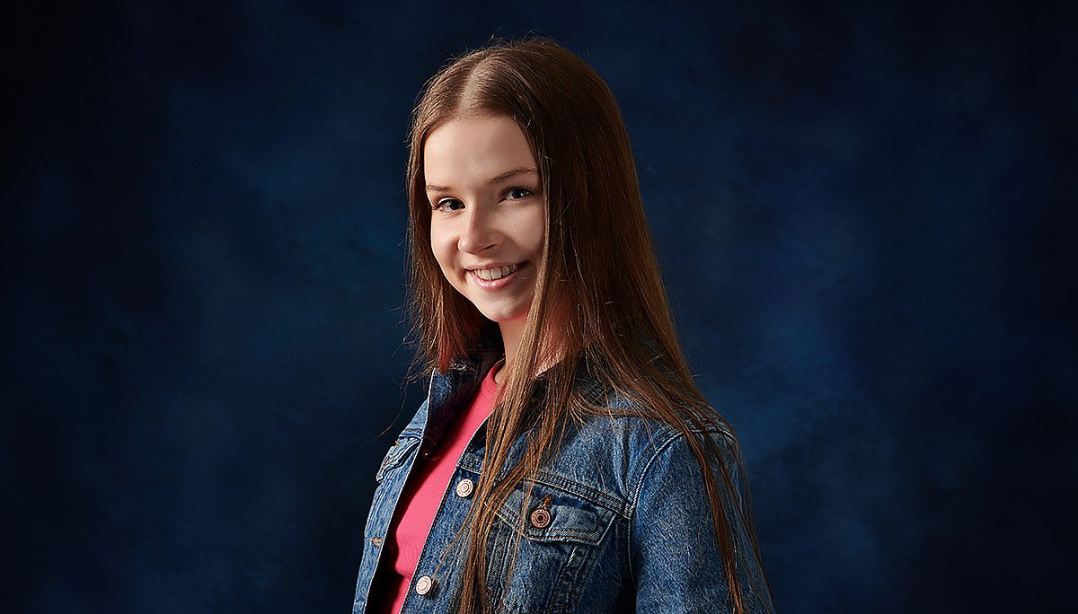 A young girl with long hair is wearing a denim jacket and a red shirt.