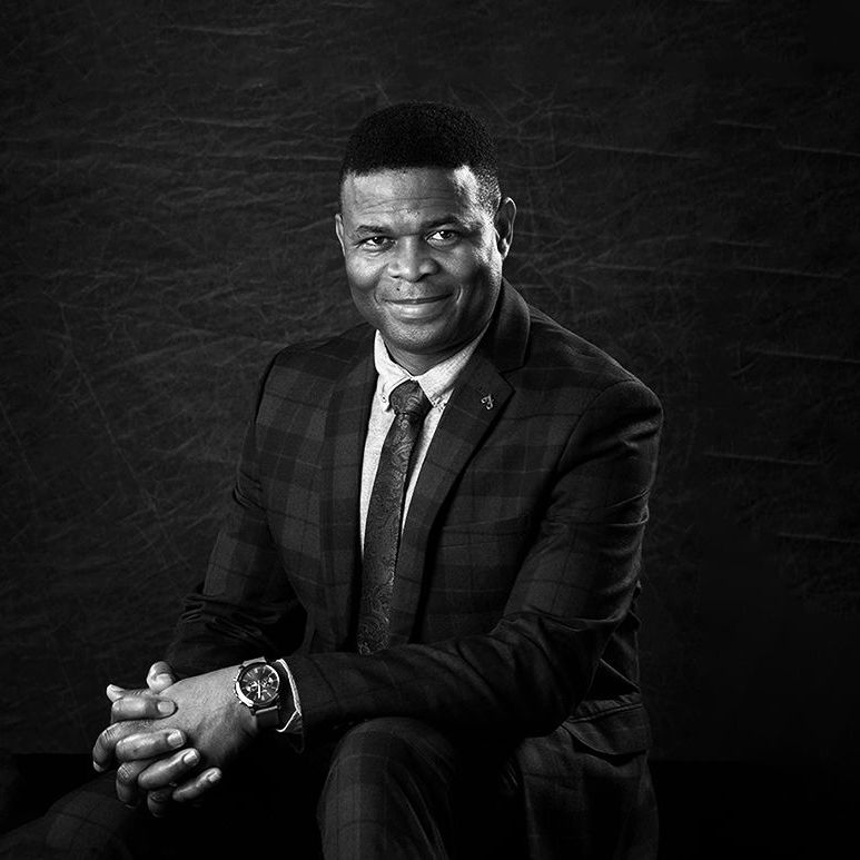 Black and white professional headshot of a man in a suit with hands folded — Oakley Studios, Luton