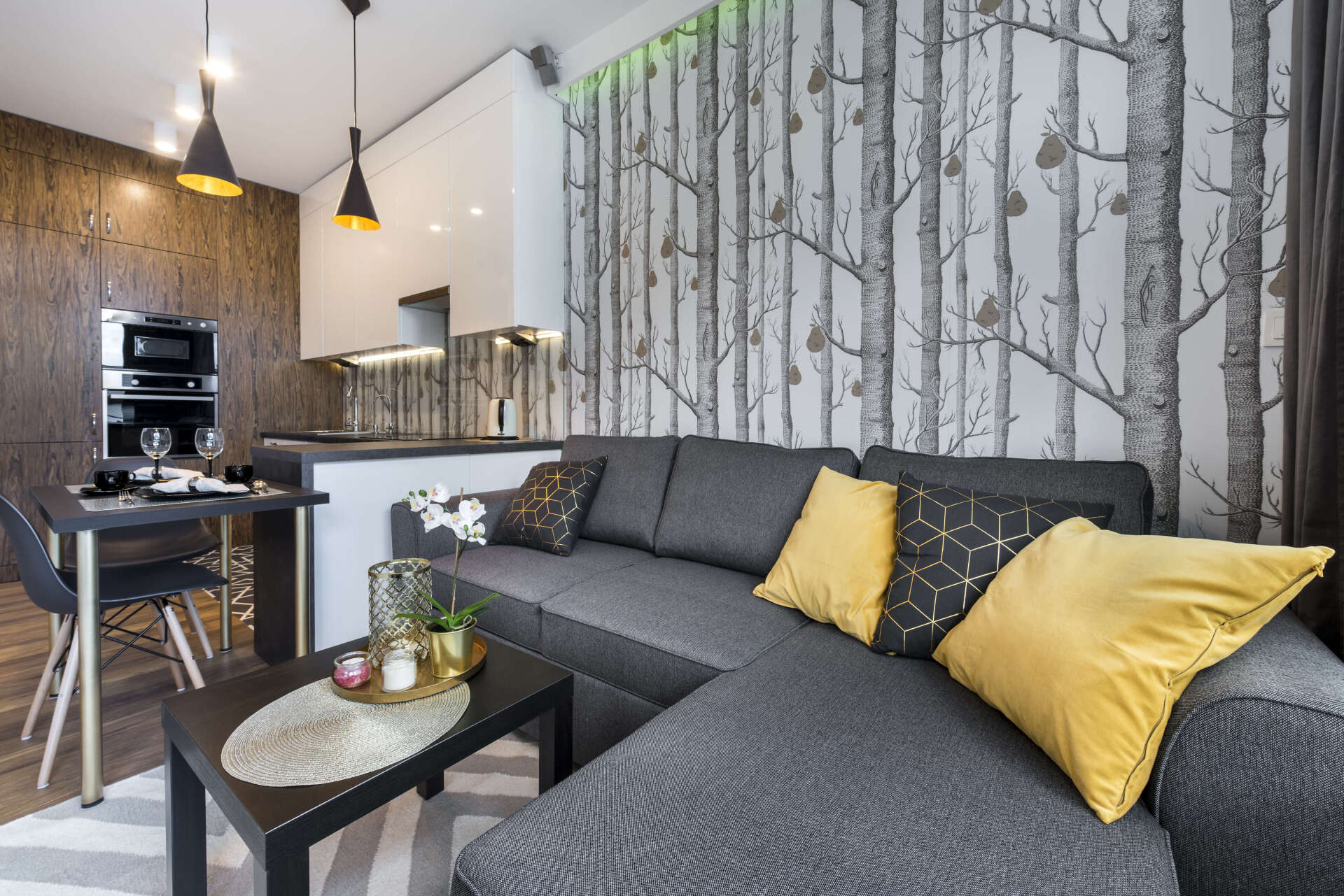 Modern gray sectional sofa in a bright living room with yellow pillows and a birch-pattern accent wall.