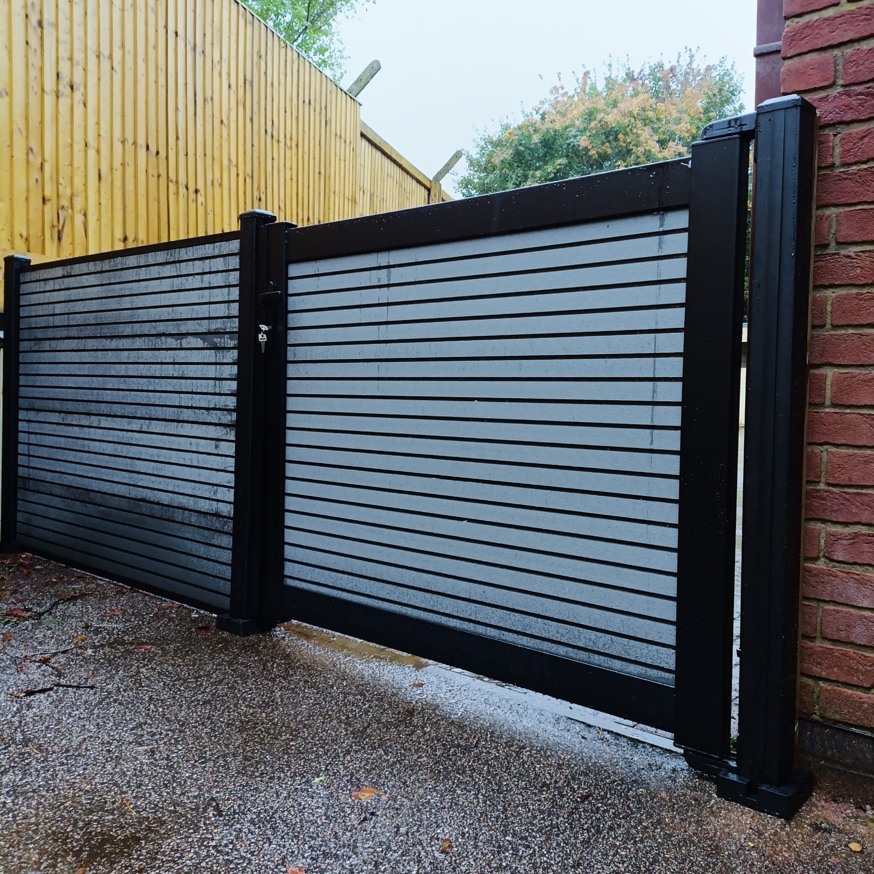Black and gray horizontal slat fence with black posts, in a residential setting.