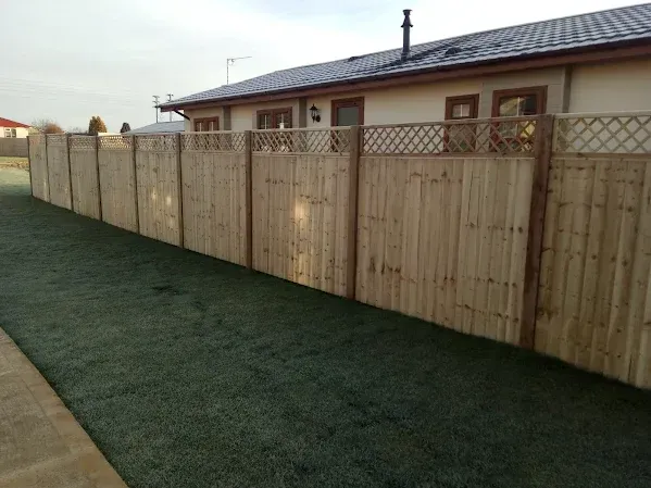 Wooden fence in a backyard with green turf and a house in the background.
