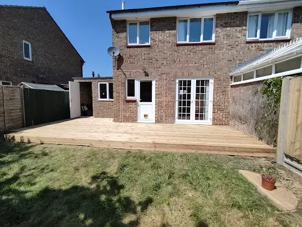 Backyard with a wooden deck, brick house, and shed on a sunny day.