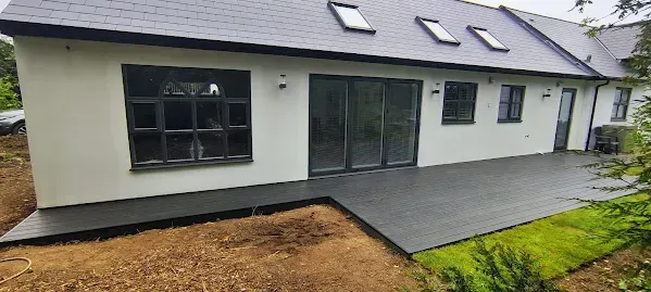 Back of a modern house with a dark deck, large windows, and a sloped roof.