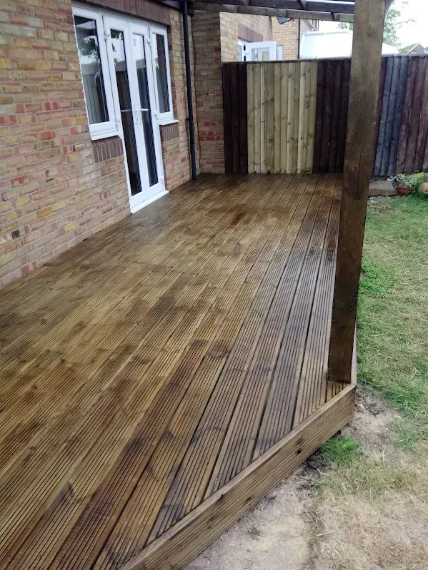Wooden deck next to brick house. Partially covered, stained wood, leading to backyard with green grass.