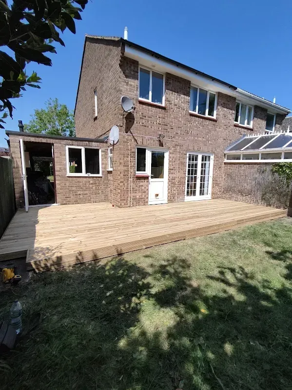 Backyard with brick house, wooden patio, and shed on a sunny day.