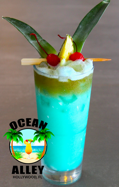 A tall glass of ocean alley cocktail with pineapple and cherry garnish