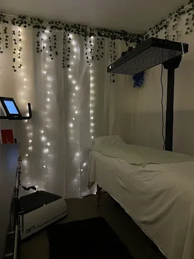 Massage room with a treatment table, soft white curtains, string lights, and hanging greenery