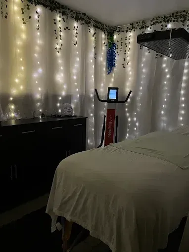 Small bedroom with fairy lights, a bed, dresser, and a red exercise machine against white curtains.