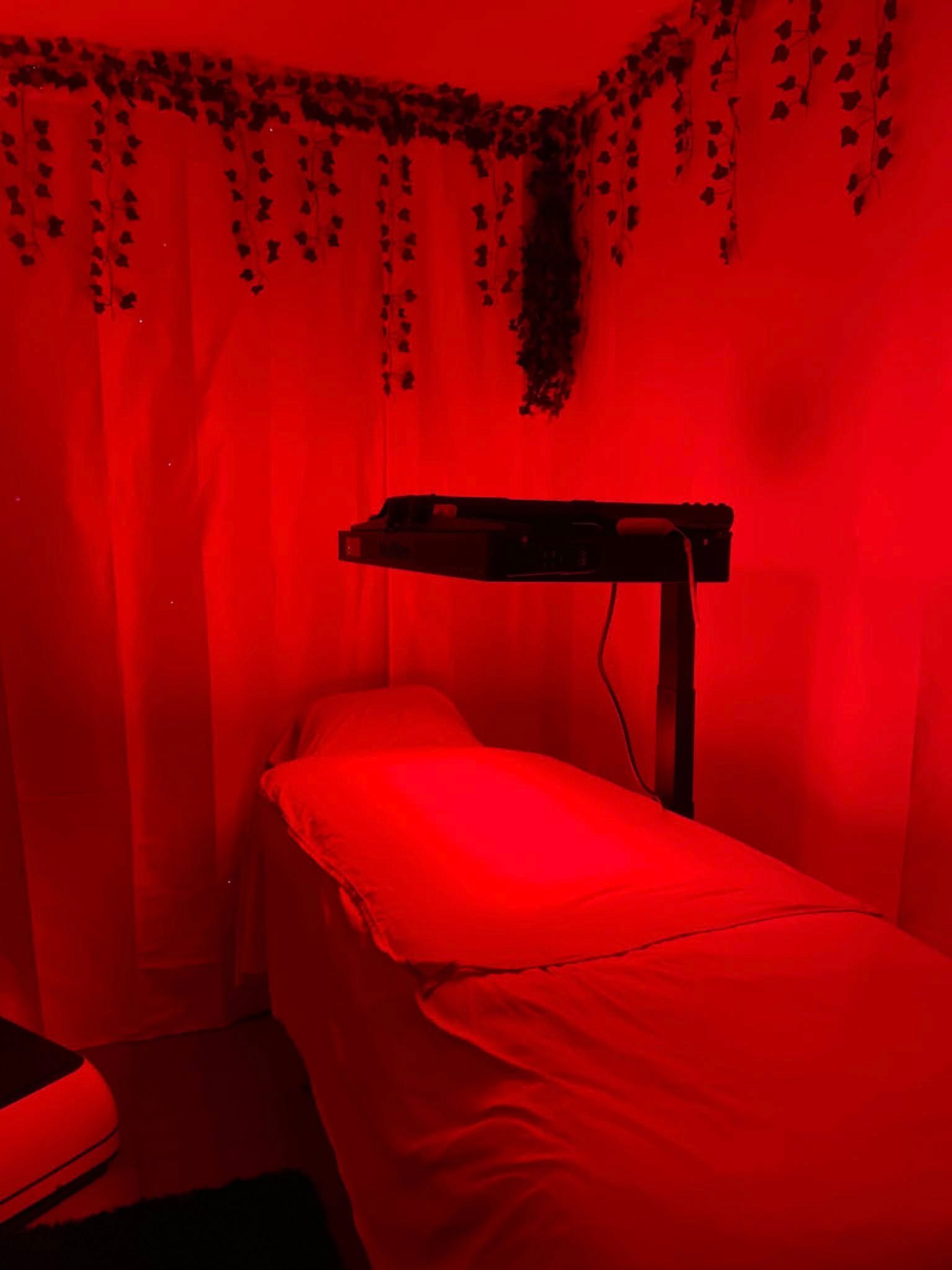 Red-lit massage table with a heated blanket in a small room, vines hanging from the ceiling.