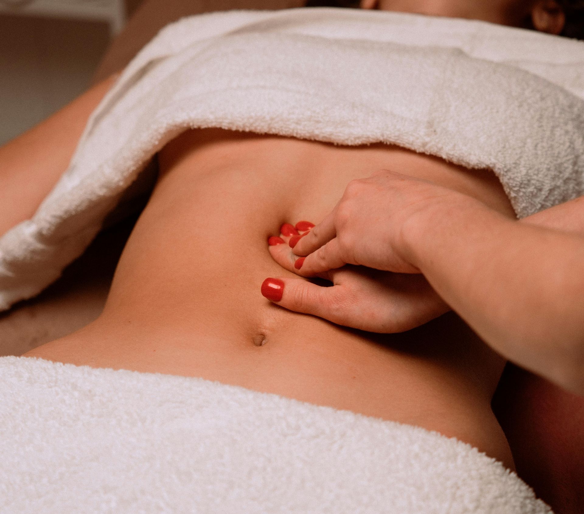 Hand plucking a small red string from a bare abdomen under a white towel